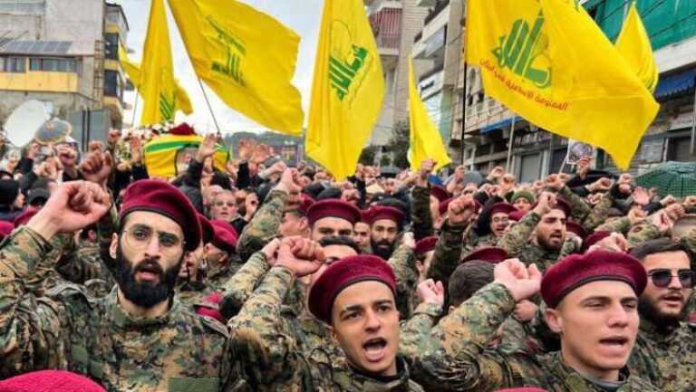 Integrantes do Hezbollah em uniformes militares marcham com bandeiras do grupo ao fundo.